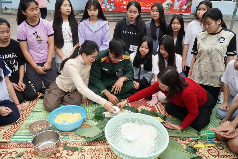 Đại úy Nguyễn Đình Thế - Chính trị viên phó Tiểu đoàn 2, Lữ đoàn 654 hướng dẫn các bạn lưu học sinh Lào gói bánh chưng, bánh tét truyền thống của Việt Nam. Ảnh: Hồ Lài