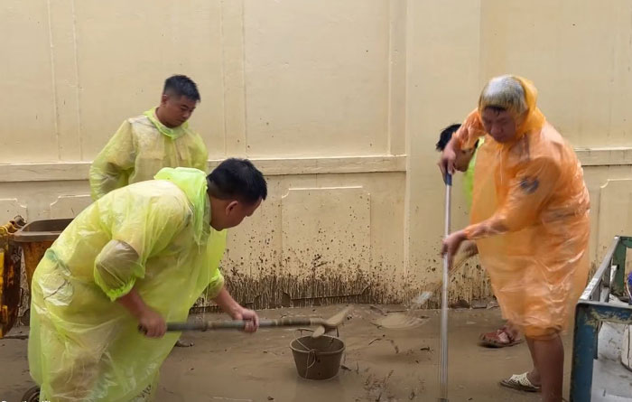 Cảnh sát giao thông dùng cuốc, xẻng dọn bùn, làm sạch môi trường. Ảnh: Công an