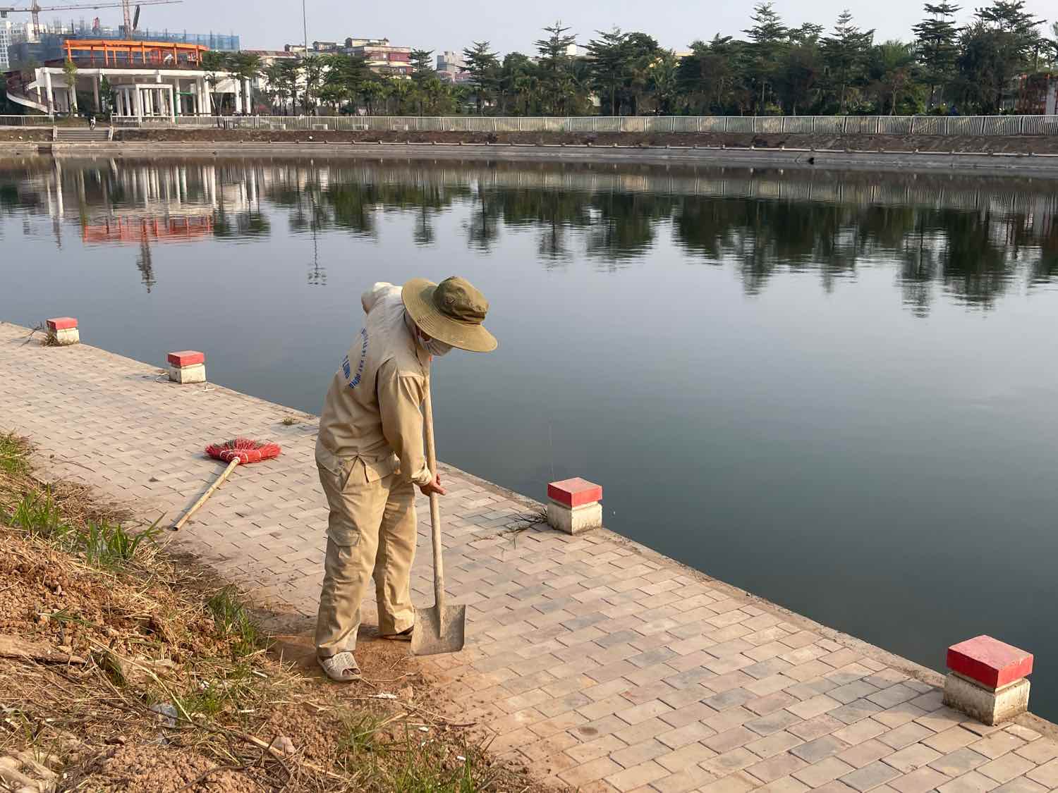 Công nhân thu gom đất cát, làm sạch khu vực vỉa hè ven hồ điều hòa. Ảnh: Khánh An